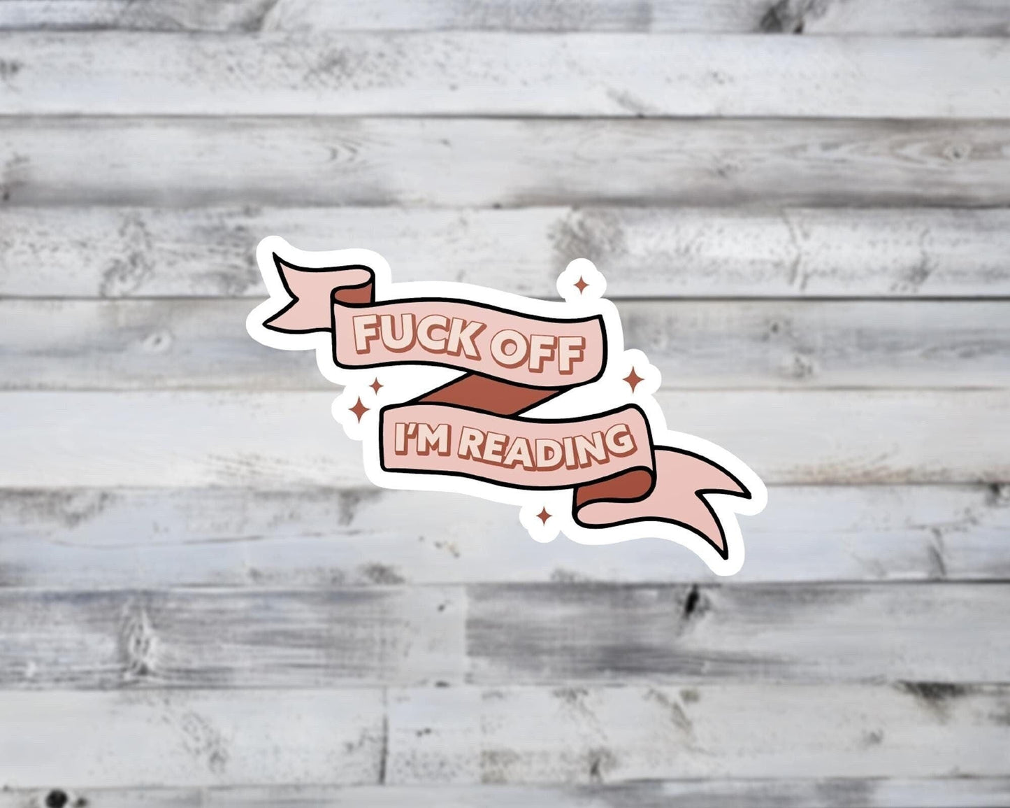 Sticker with 'F*ck off, I'm reading' text on a wooden background
