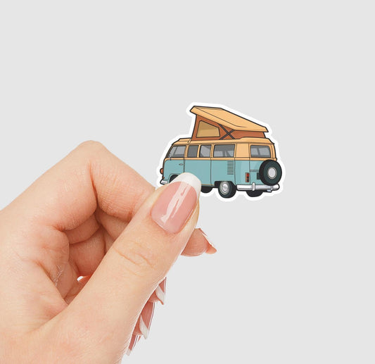 Hand holding a sticker of a vintage camper van with an open roof on a light gray background