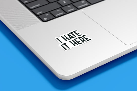 Laptop with a sticker reading 'I HATE IT HERE' on a blue background