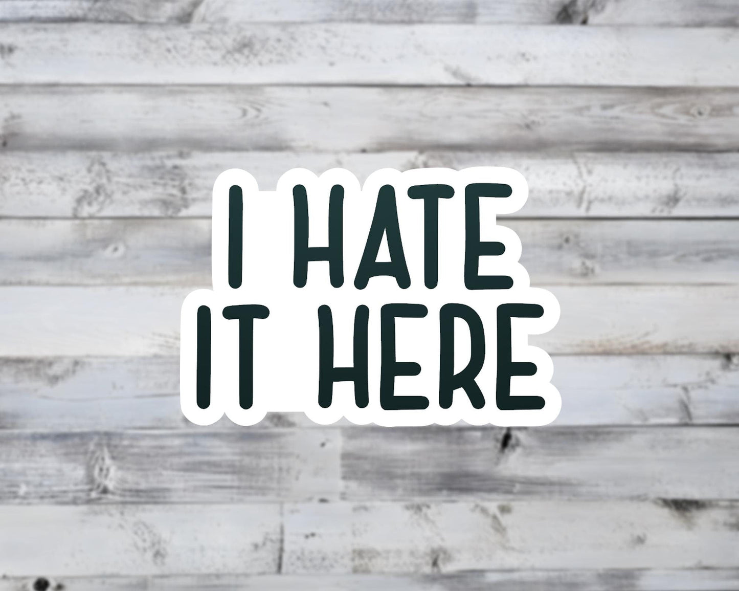 Sticker with 'I HATE IT HERE' text on a wooden background