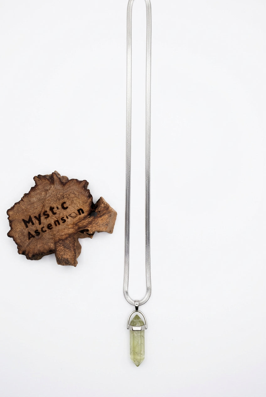 A silver-toned snake chain necklace with a clear crystal pendant, displayed next to a rustic wooden tag engraved with 'Mystic Ascension' on a light gray background.
