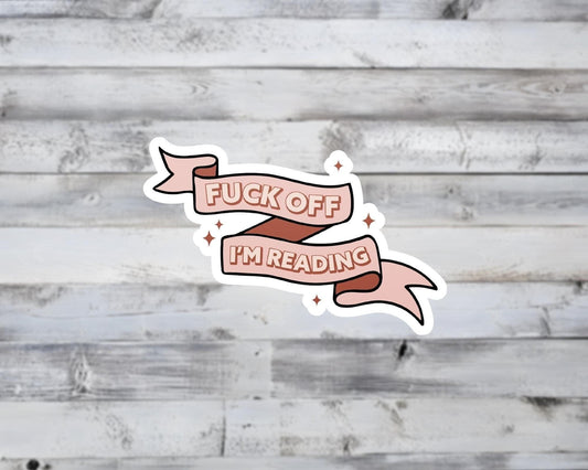 Sticker with 'F*ck off, I'm reading' text on a wooden background