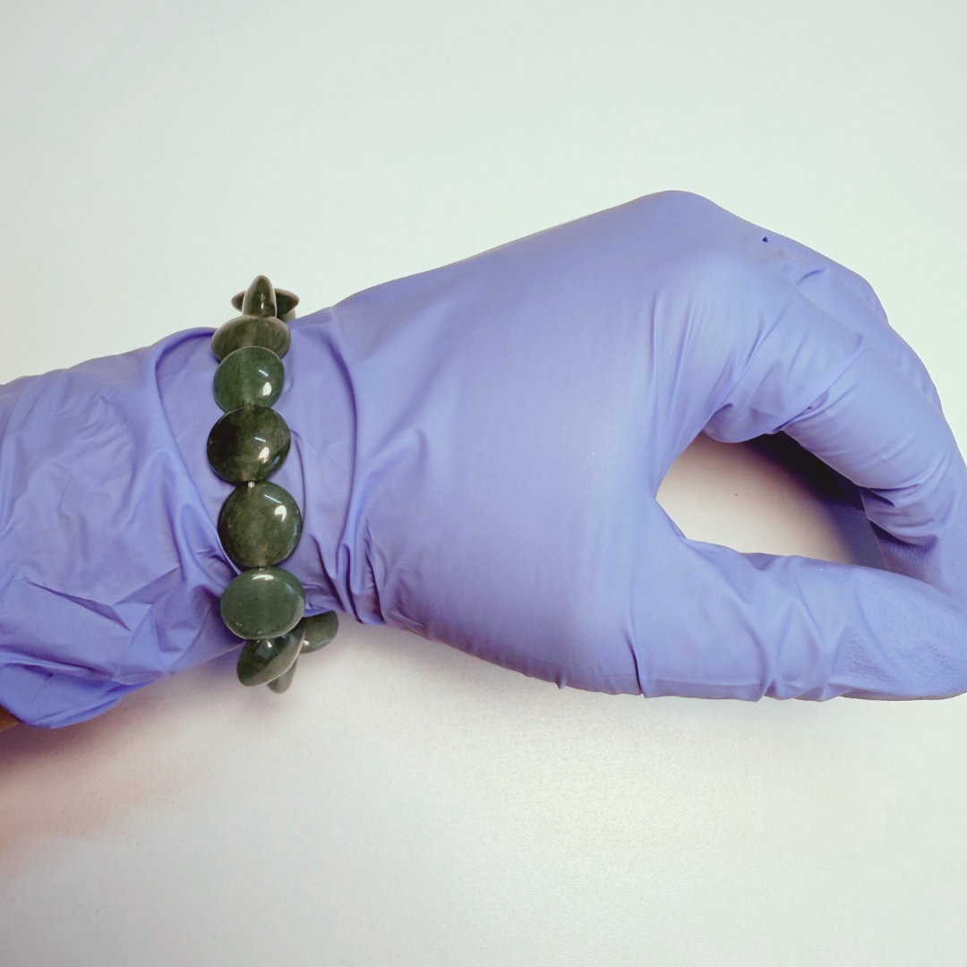 Hand wearing a purple glove holding a green beaded bracelet on a white background