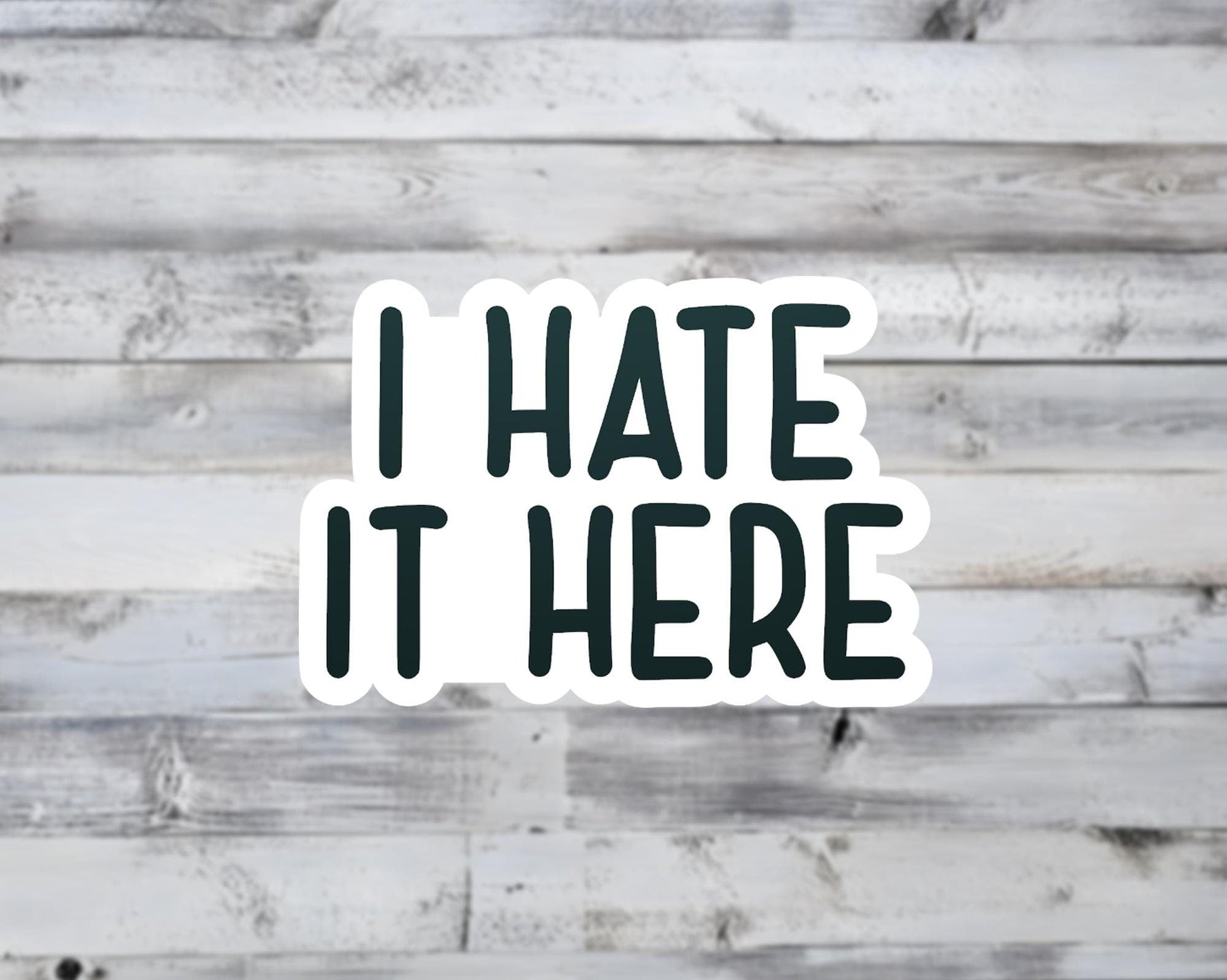 Sticker with 'I HATE IT HERE' text on a wooden background