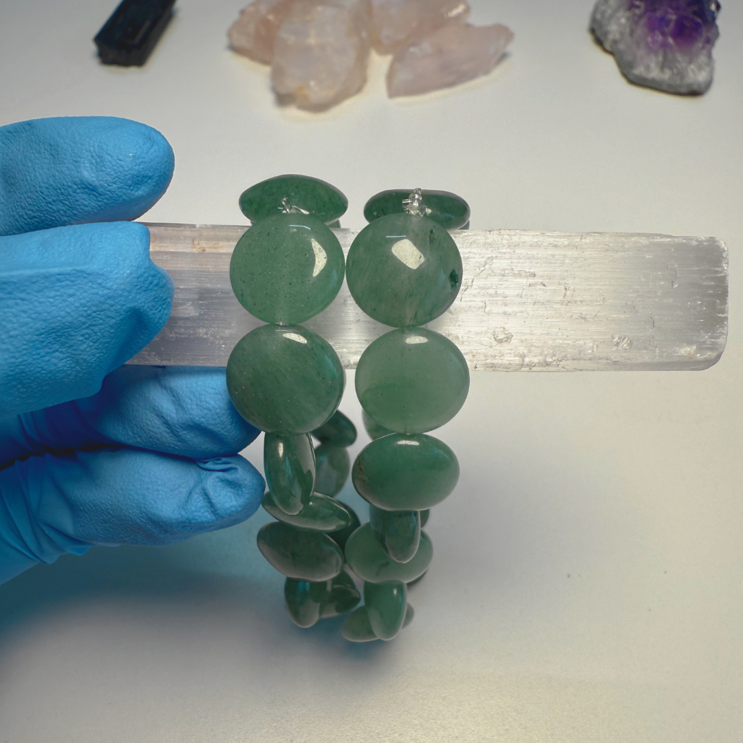 Green gemstone bracelet held by a gloved hand with crystals in the background