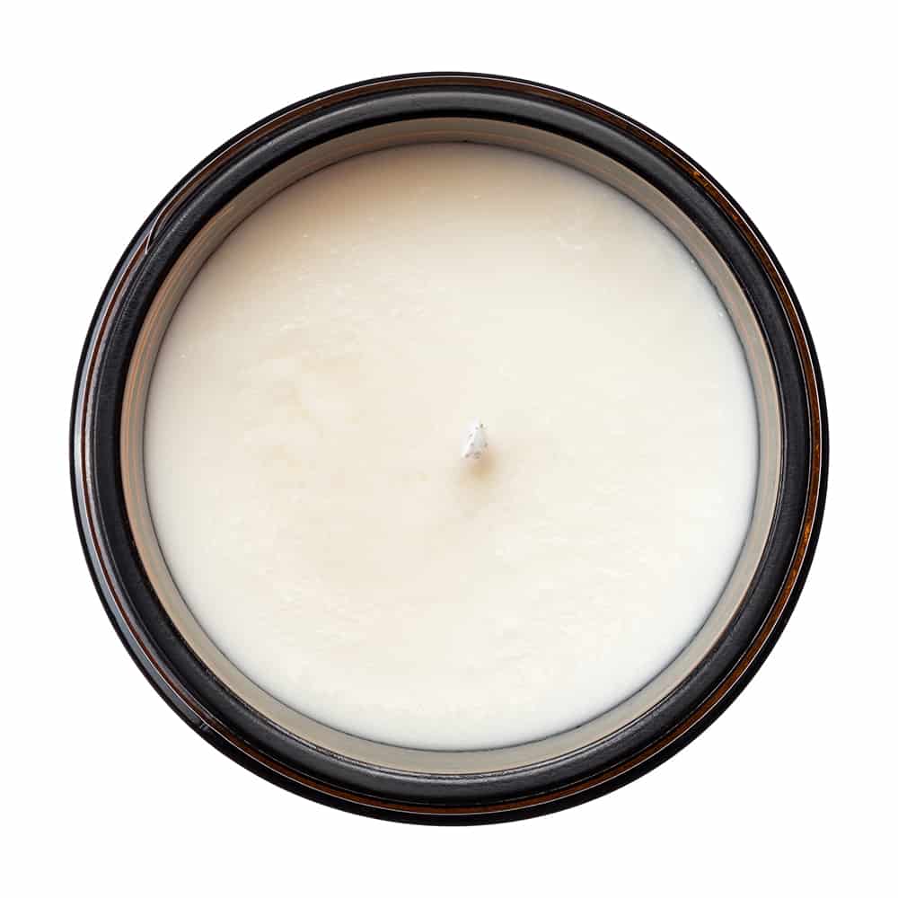 White candle in a round container with a dark brown rim on a white background